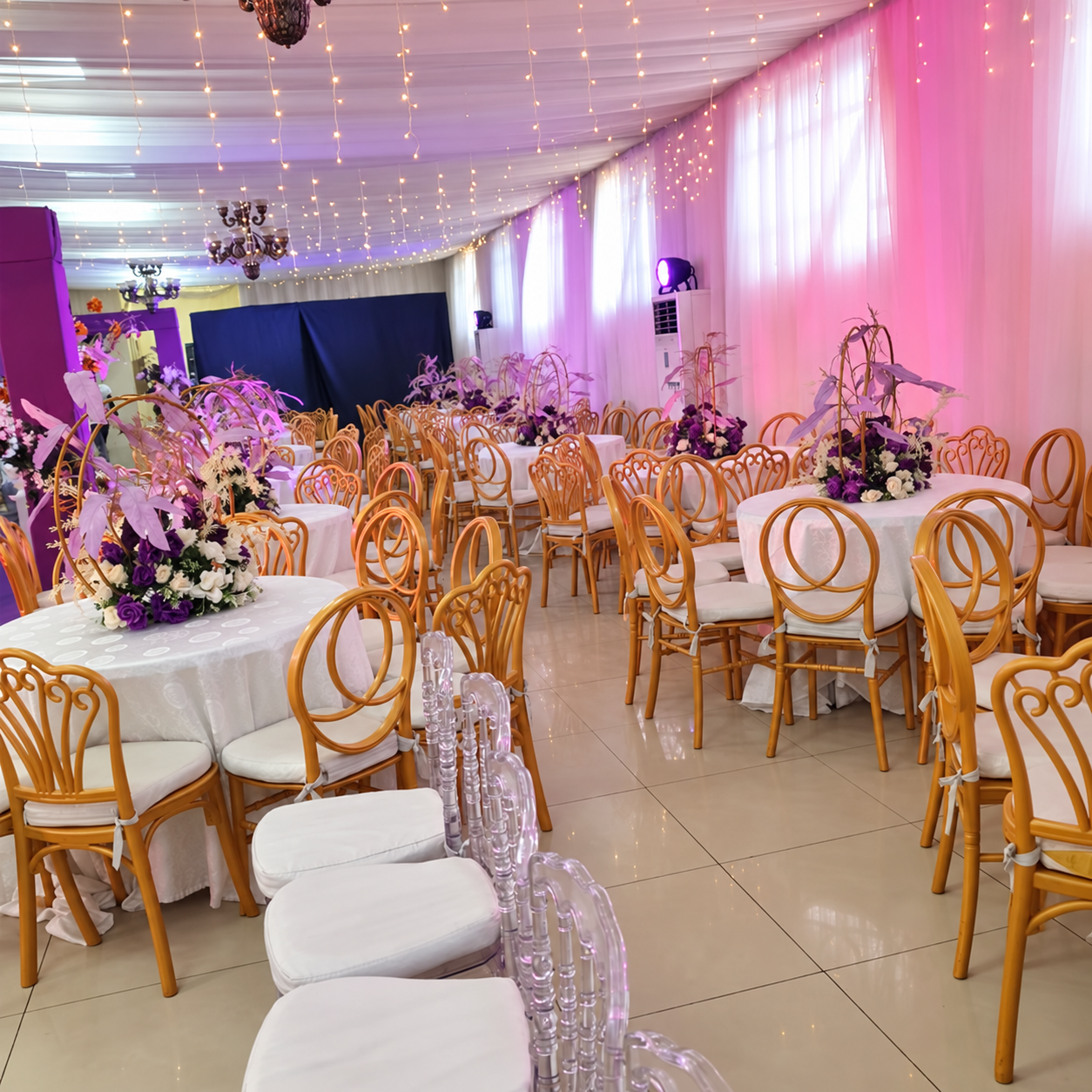 Gold chairs and round tables beneath draped ceilings and decorative lights